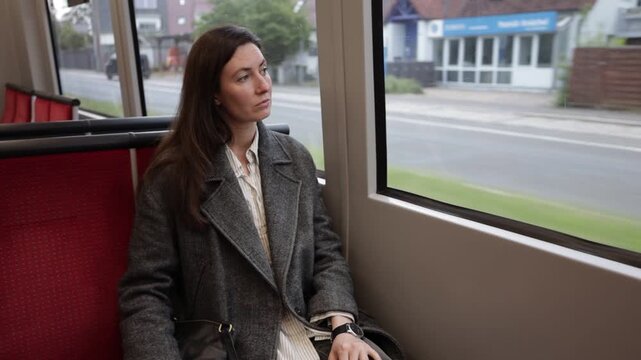 Woman looking out train window during commute, thoughtful expression, urban scenery passing by