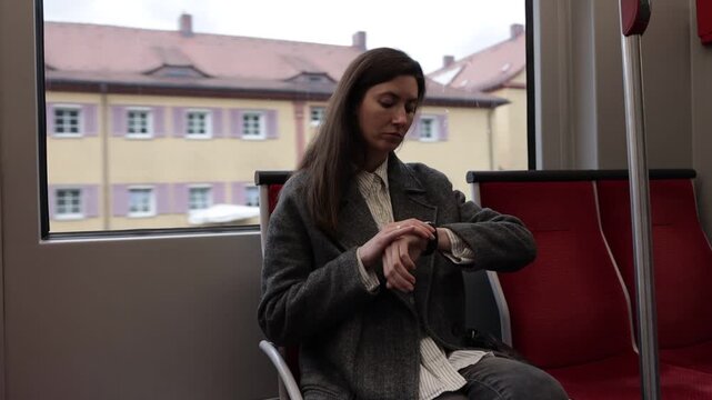 A woman waiting in a train, glancing at her watch with a thoughtful expression