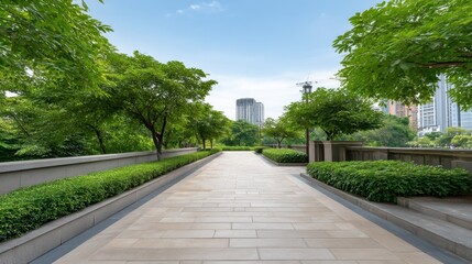 Obraz premium Serene Urban Pathway Surrounded by Lush Green Trees and Bushes with City Buildings under Clear Blue Sky in a Peaceful Environment