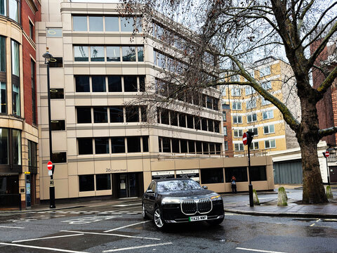 Luxury BMW i7 driving on wet city street in London, UK past office buildings and bare trees