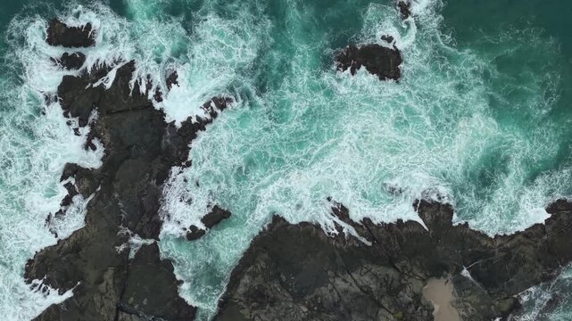 Aerial view of turquoise waves crashing against dark volcanic rocks at Siung Beach in Tepus, Special Region of Yogyakarta, Indonesia.