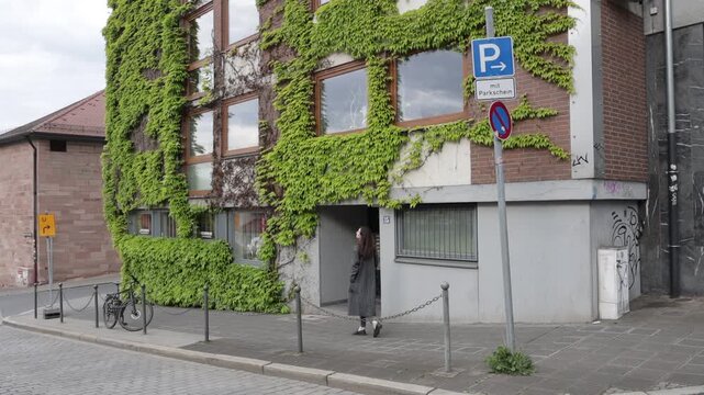 Woman walking past ivy-covered building with parking signs and bicycle