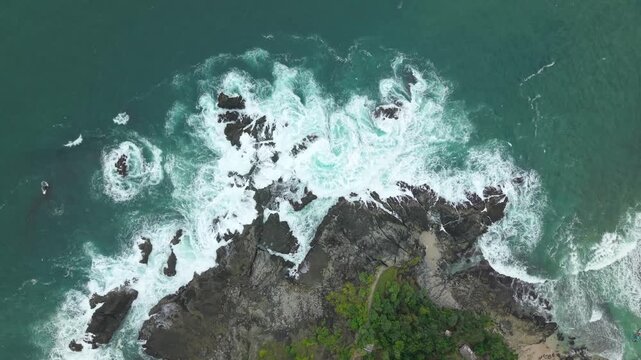 Aerial view of Siung Beach where turquoise ocean waves crash against dark jagged rocks and white foam swirls around the coastline Tepus, Special Region of Yogyakarta, Indonesia.