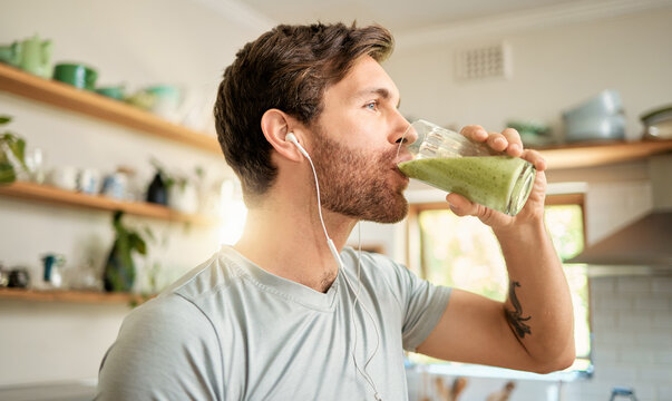 Wellness, earphones and man in home with smoothie, organic juice and protein shake for gut health. Fitness, person and audio tech in kitchen with green drink, supplement and exercise tips in podcast