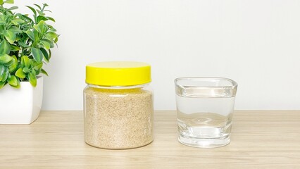 A jar of psyllium husk next to a glass of water on a wooden surface. A simple composition illustrating the daily use of soluble fiber for gastrointestinal support. © Lisi4ka