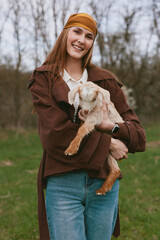 Fototapeta premium Joyful woman outdoors with a goat kid, sharing a warm moment in a rustic lifestyle setting. A candid scene of care, companionship, and natural farming vibes in a grassy field.