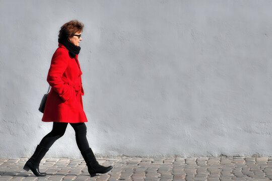 confident woman in striking red coat walks along cobbled street exuding elegance and style