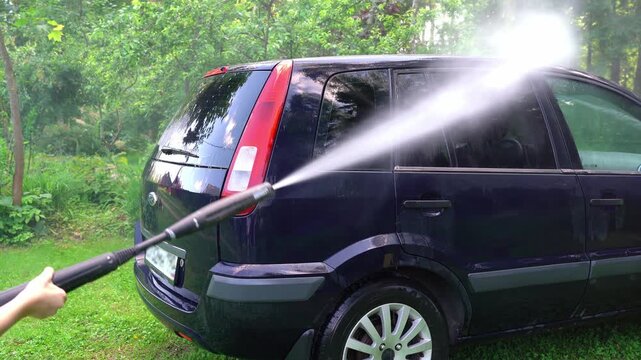 Washing car with pressure washer outdoors in nature. High pressure car wash
