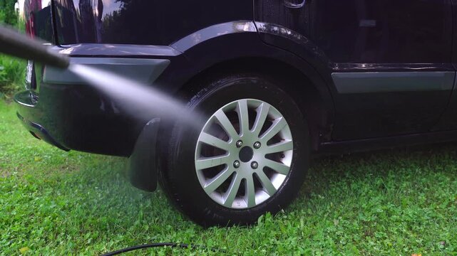 Washing car wheel with pressure washer outdoors. High pressure car wash. Car wash