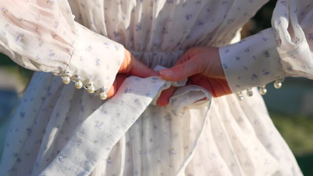 Hands dress tie woman tying a bow behind her back on a floral vintage dress while preparing for a romantic summer day