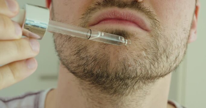 man applying liquid drops to patchy beard areas for facial hair growth and beard care. Ideal for grooming, beard serum, skincare, cosmetic treatment, self-care, and men&rsquo;s wellness concepts.