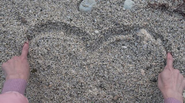 Sand heart drawing woman sketching a romantic symbol on a pebble beach with her fingers during a cold day