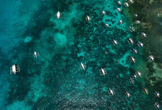 Aerial drone view of traditional Filipino outrigger boats floating above vibrant coral reefs near Daco Island, Siargao, Philippines.