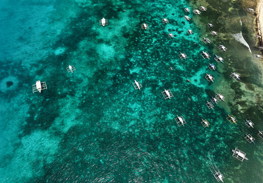 Aerial drone view of traditional Filipino outrigger boats floating above vibrant coral reefs near Daco Island, Siargao, Philippines.