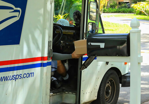 Mailman delivers a package from his vehicle into a black mailbox in a residential neighborhood in Fort Lauderdale, Florida, USA. 