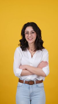 Brunette young woman pointing upward with both index fingers toward copy space, making silence gesture and crossing arms on yellow background. Vertical studio video for attention and secrecy concepts.