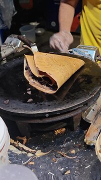 Close up of street food vendor folding a crispy chocolate cheese crepe on a hot griddle