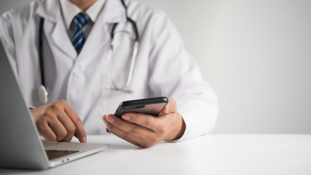 Doctor with stethoscope using smartphone and laptop for telemedicine online consultation