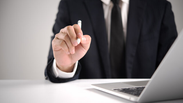 Businessman in dark suit holding digital pen pointing forward near laptop for e signature