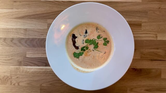 Creamy mushroom puree soup white plate on wooden table restaurant closeup, garnished with herbs and mushroom slice, warm natural