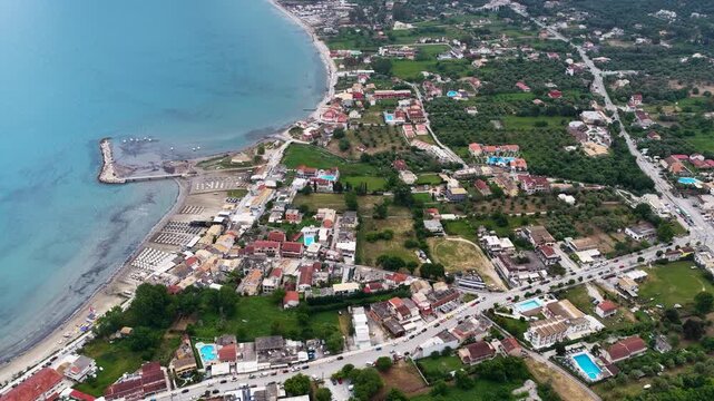 Aerial view of Roda beach and village in North Corfu Greece, showcasing the beautiful coastline, clear Ionian Sea, small pier, beachfront hotels, and lush green landscape from a drone.