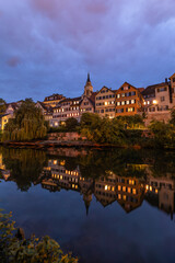 Naklejka premium 19.05.2026: Traditional half timbered houses illuminated at dusk, reflecting perfectly in the calm water of Neckar river in Tuebingen, Germany.