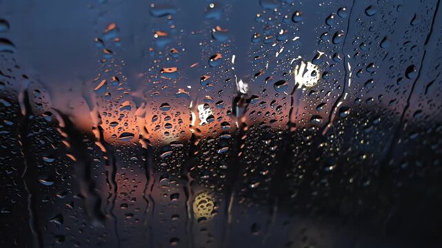 Raindrops sliding down window glass against dark twilight sky