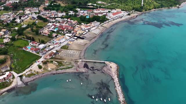 Aerial panorama of Roda village coastline in North Corfu, Greece. Drone view of Ionian sea, sandy beach, sunbeds, hotels, and breakwater pier on a summer vacation.