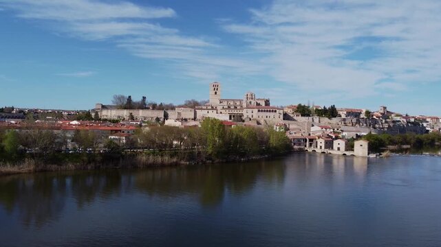 4K aerial drone video ascending from the Duero River to reveal the stunning medieval skyline of Zamora, Spain. The rising shot elegantly captures the historic old town, Romanesque Cathedral, and ancie