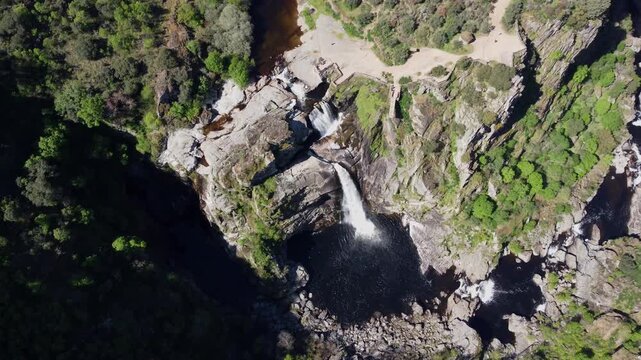 K cinematic top-down aerial drone video orbiting above the impressive Pozo de los Humos waterfall in Salamanca, Spain. The nadir shot captures the water plunging into a dark pool, surrounded by rocky