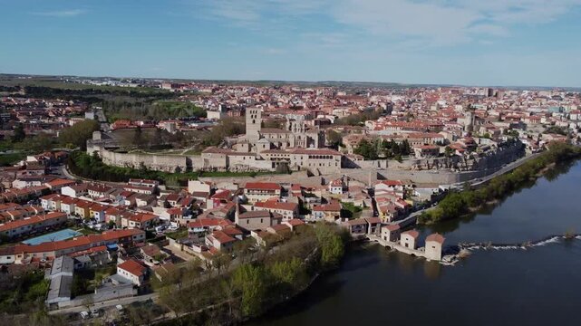 4K drone video ascending over the historic center of Zamora, Spain. It shows the medieval cathedral, the castle, the old city walls, and the Duero River flowing by on a clear sunny day.