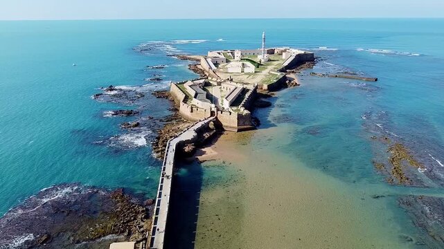 Santa Catalina fortress. La Caleta Beach. C&aacute;diz. Spain. Aerial view. View of a 17th-century military fortification next to a sea of ​​vibrant colors and waves crashing against the rocks.