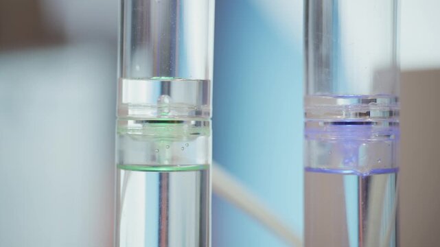 Transparent hydrogen research cylinders with blue and green glowing fluids during electrolysis process for renewable energy and low emission fuel technology