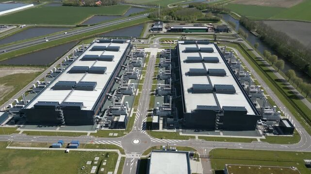 Aerial side perspective of a large cloud computing datacenter facility with cooling systems and industrial architecture located in the Dutch countryside.
