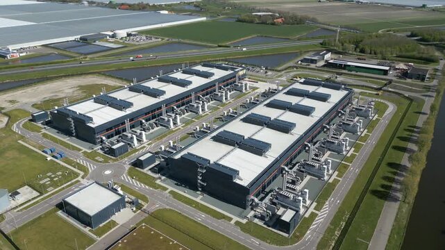 Cinematic aerial drone footage of a large modern datacenter and server infrastructure complex surrounded by roads, canals and Dutch farmland in the Netherlands.