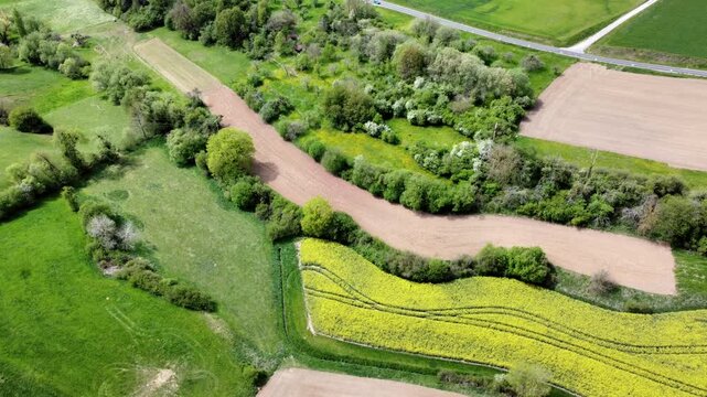 Drohne fliegt &uuml;ber vielf&auml;ltige Agrarlandschaft im Fr&uuml;hling, Rapsfeld, Streuobstwiese, Landwirtschaft, Luftaufnahme, Bayern
