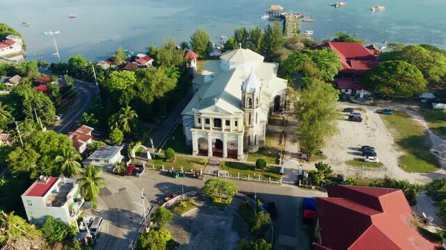 Dauis Church and coastal neighborhood under bright tropical sunlight, drone orbit right to left in morning
