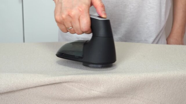 Hand removes pills from knitted clothing using fabric shaver. Textile pilling. Linting. Fabric lint, pilly, pellet, fluff. Fluff-ball remover