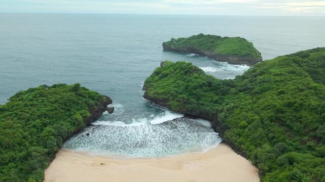Aerial view of Sedahan Beach with its white sand and turquoise waves surrounded by lush green cliffs in Girisubo, Special Region of Yogyakarta, Indonesia.