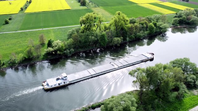 Drohne fliegt &uuml;ber Fluss mit Binnenschiff, Ufer mit Auwald und Agrarland, Luftaufnahme