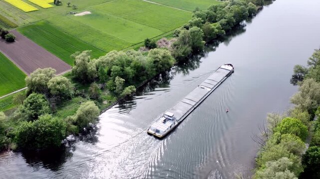 Drohne fliegt &uuml;ber Fluss mit Binnenschiff, Ufer mit Auwald und Agrarland, Luftaufnahme