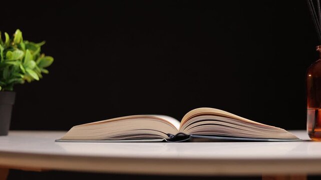 Open book with pages gently turning on a white table with a plant and diffuser