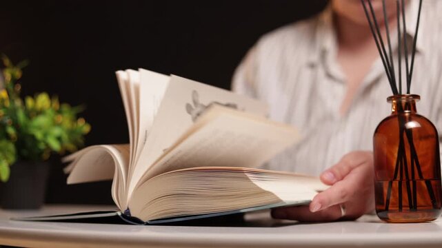 Person turning pages of an open book with a diffuser and plant nearby