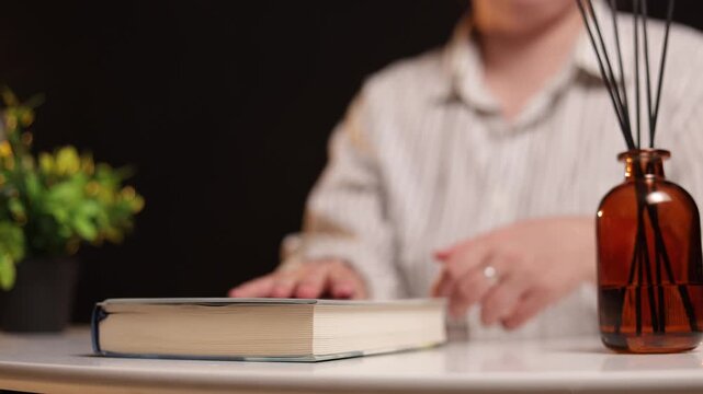 Person placing a book next to a reed diffuser and plant on a table