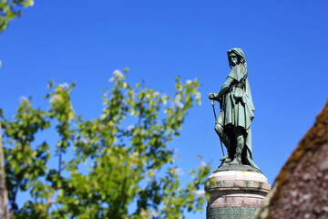 Das historische Vercingétorix-Monument von der Seite auf seinem Sockel, umrahmt von grünen Blättern vor einem wolkenlosen, tiefblauen Himmel. © fotoping