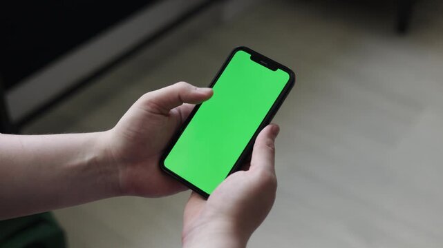 Person holding a smartphone with a green screen for customization