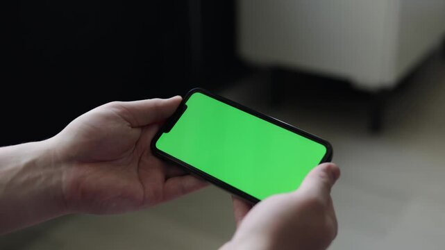 Close-up of hands holding a smartphone with a green screen display
