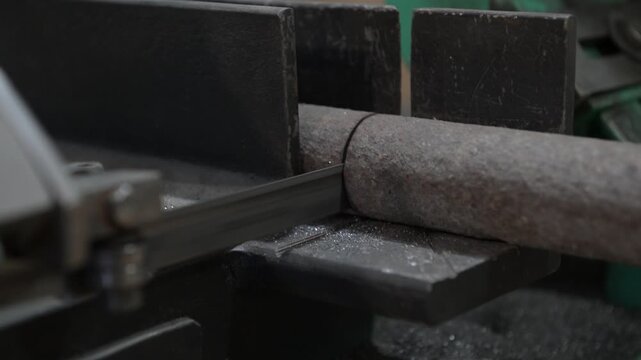 The lathe is located in the production hall. An electric metal cutting machine saws off a piece of metal covered with rust with an automatic hacksaw to make a close-up product