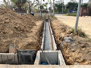 Fototapeta premium Concrete drainage channel construction along a rural roadside with excavation trench, infrastructure development, stormwater management system, and civil engineering work in progress.