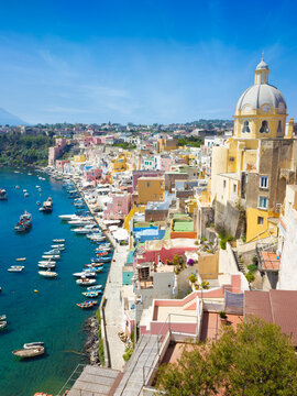Colorful houses and boats in Marina Corricella, Procida island, Italy in sunny day. High angle view shows historic Mediterranean town on Procida with vibrant pastel buildings and church dome